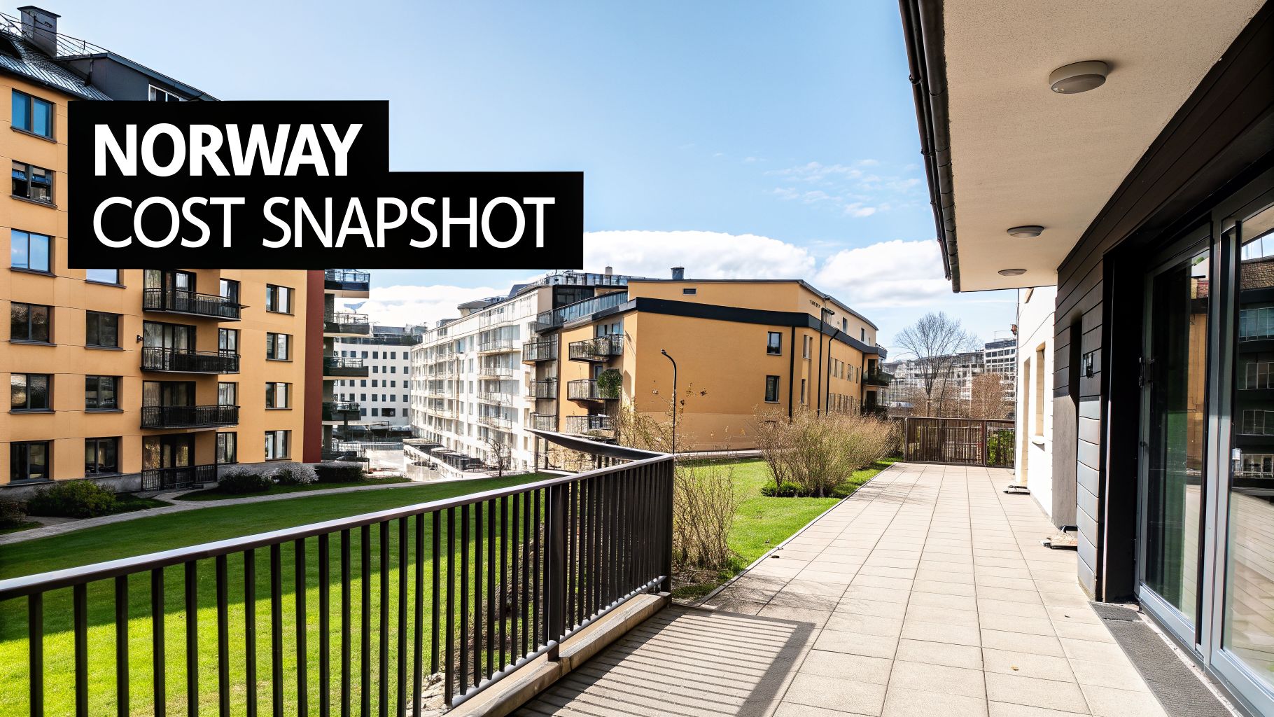 Modern apartment buildings with balconies overlook a green lawn and paved terrace on a sunny day.