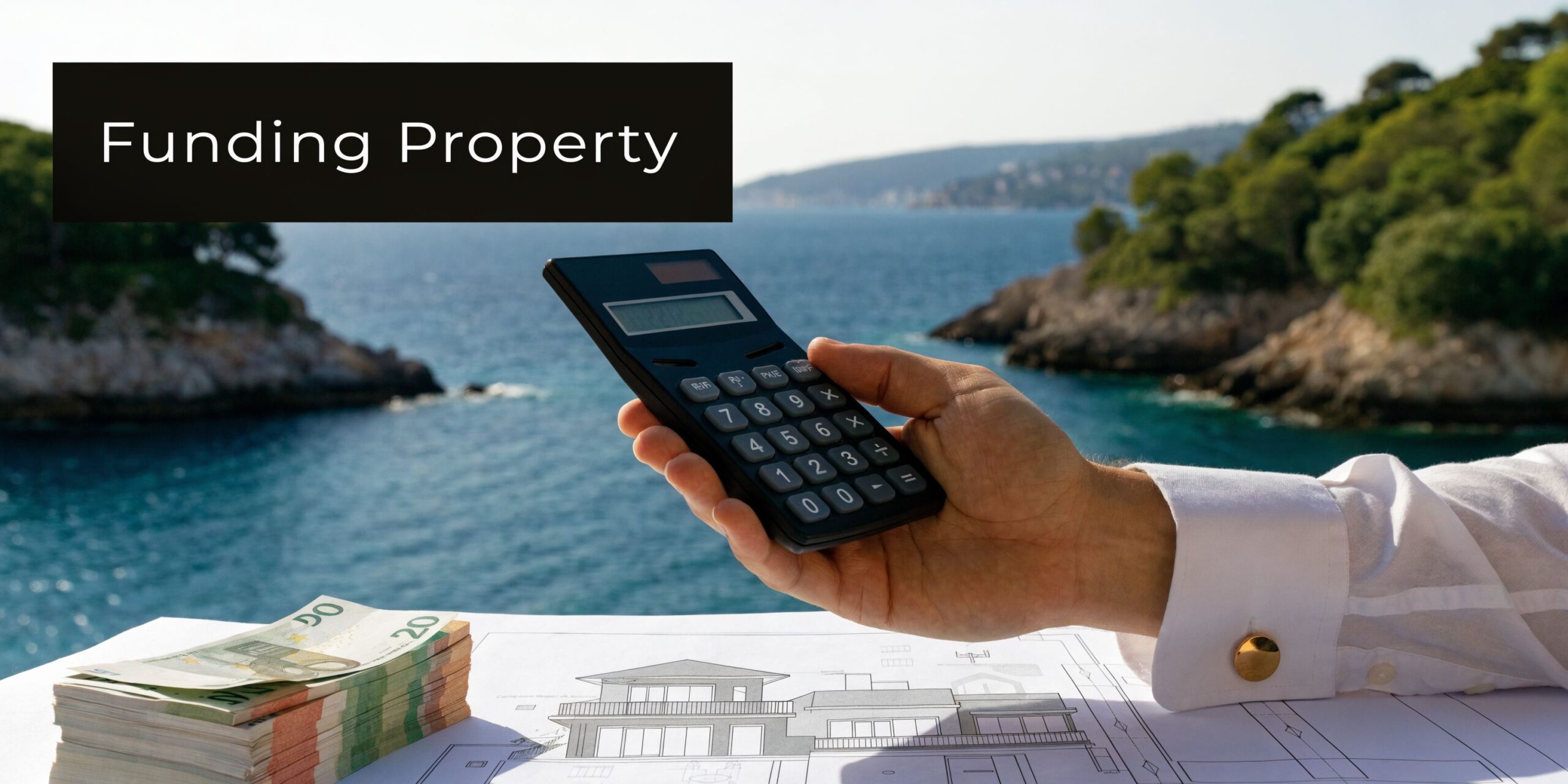 A person holds a calculator over house blueprints and a stack of Euro banknotes near the ocean.