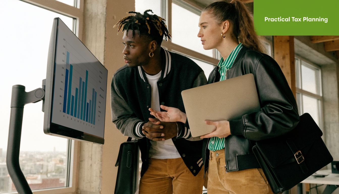 Two professionals looking at a large wall-mounted monitor displaying financial data and bar charts in an office.